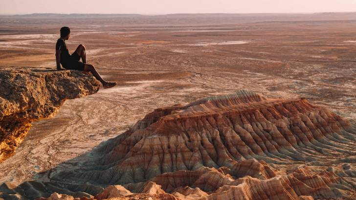 man sitting on a cliff overlooking the desert