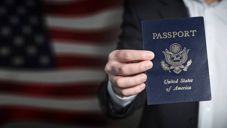 man holding a passport with the american flag in the back ground