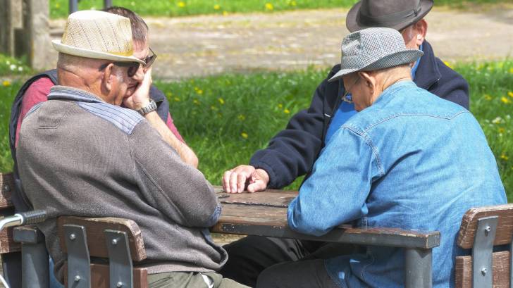 4 old men playing a game of dominos around a table outside