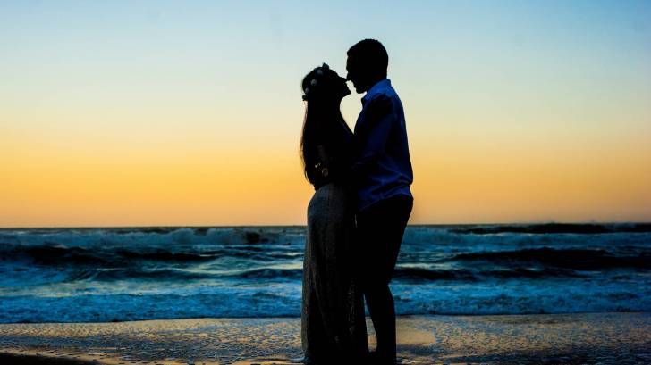 pregnant husband and wife on a beach at sunset in a silhouette