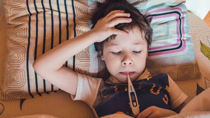 young boy in bed with a thermometer taking his temp