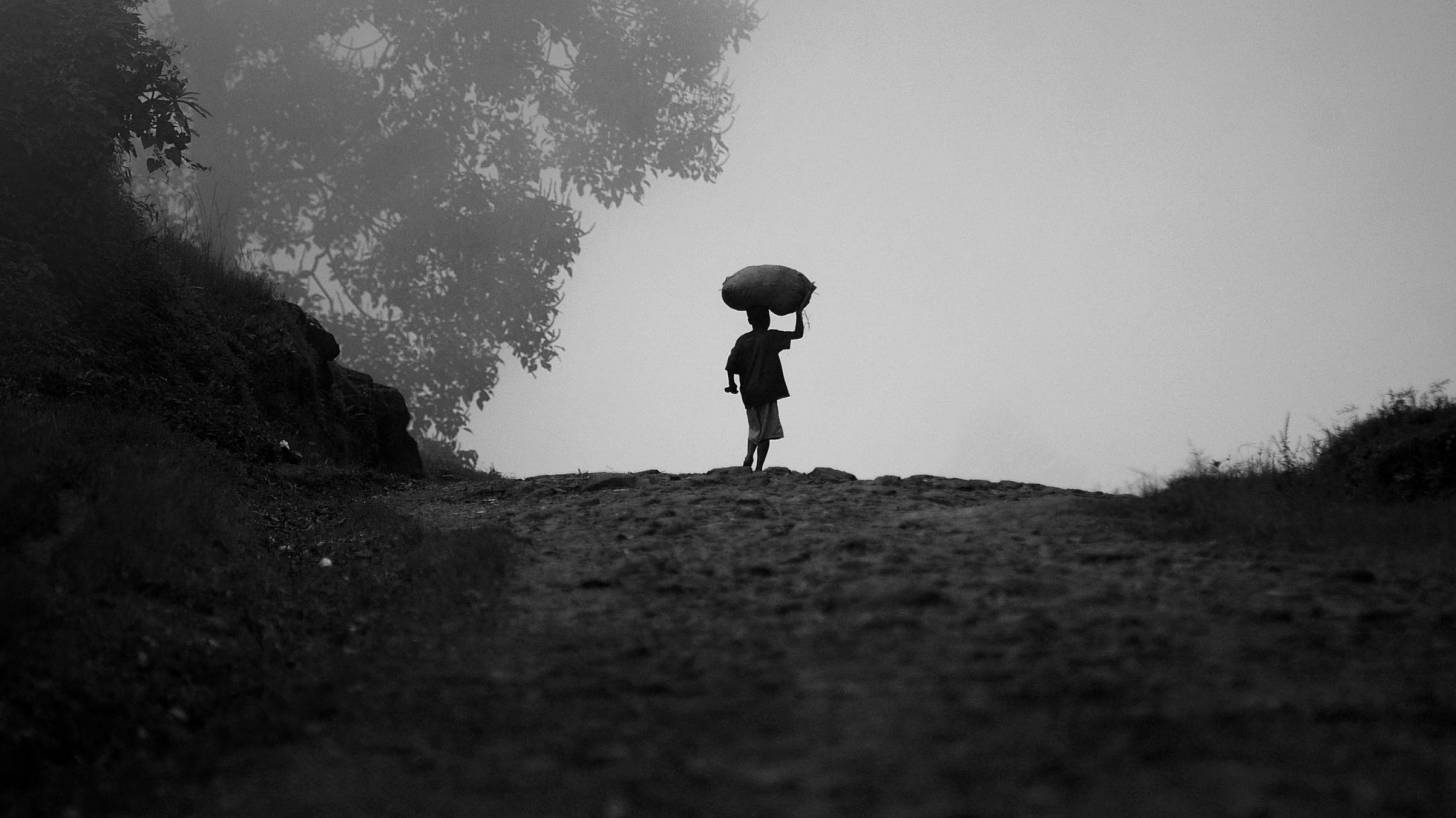 child in uganda walkng with food on his head thru the mist