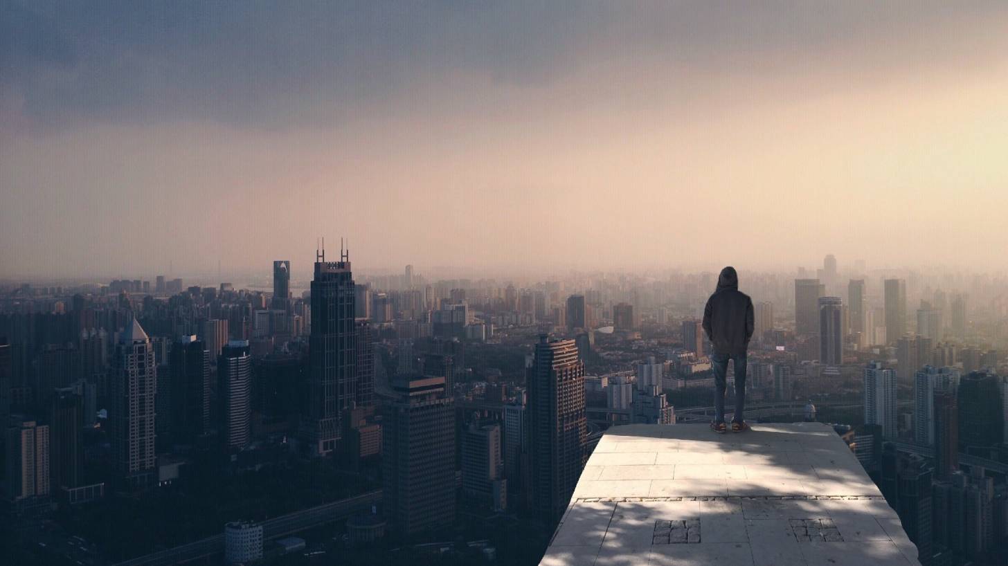 man standing on the edge of a building looking over the city