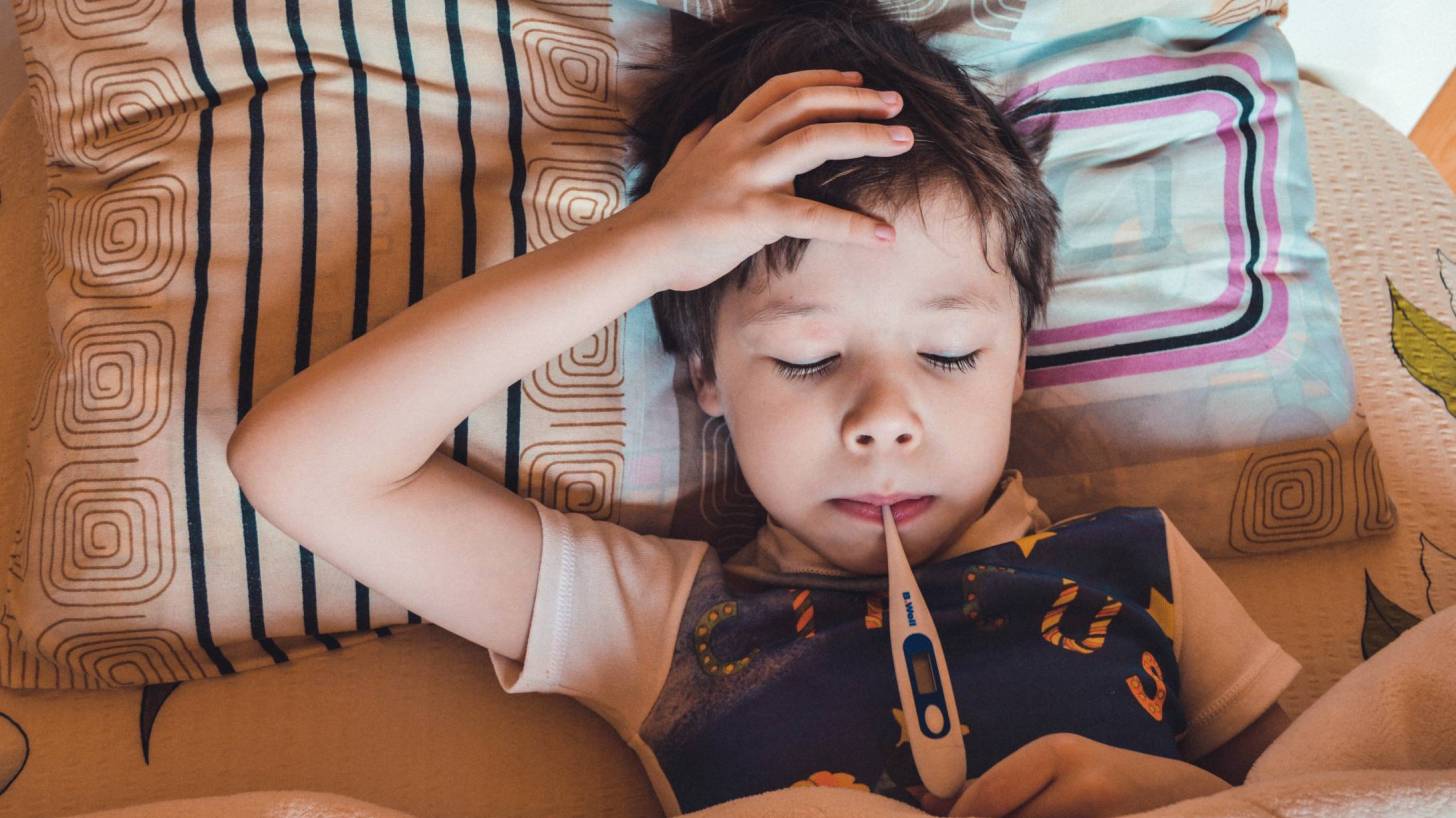 young boy in bed with a thermometer taking his temp