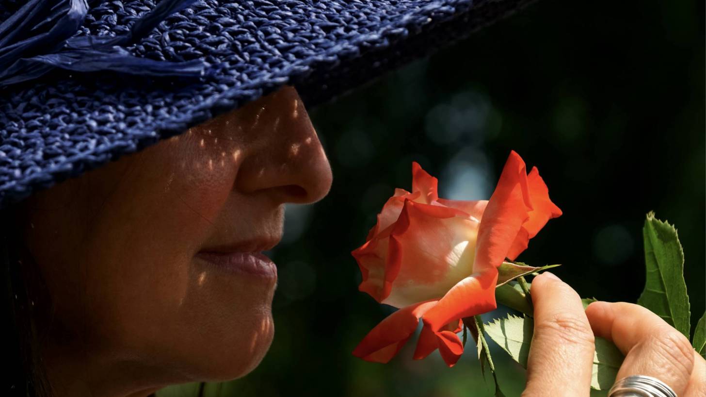 woman in blue hat smelling a flower