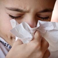 young boy sneezing into a tissue