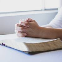 hands folded on a bible saying prayers